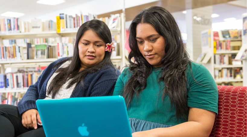 Two women use a laptop at a library.