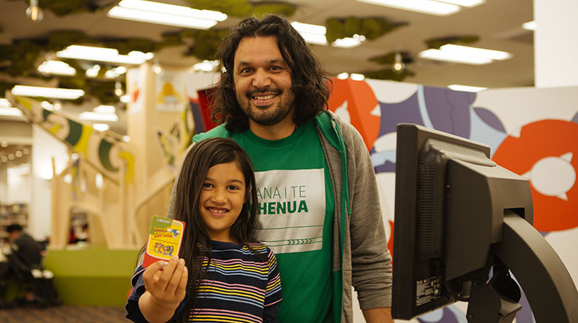 Library card competition: Image of man with young girl inside library.