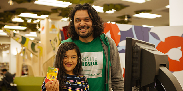 Image of an adult and a girl holding up a library card.