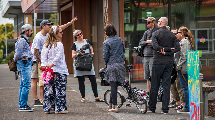 A group of people outside, one using recording equipment while another seems to be interviewed.