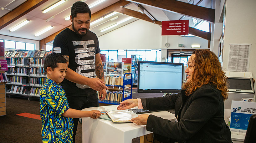 Child and parent in a library smile as they receive a new library card from staff.
