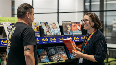 A smiling librarian handing a book to a customer..