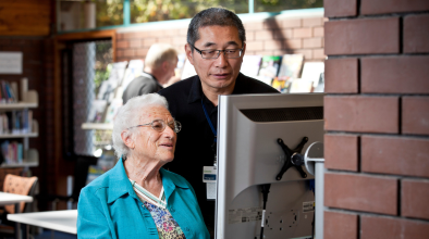 Photo of a librarian helping a customer to use a library computer.