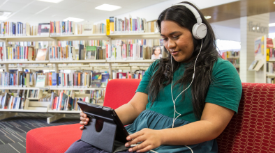 Photo of a woman smiling while watching media on an iPad at a library