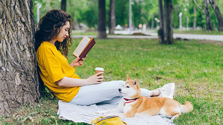 A woman reading against a tree in the company of her dog.
