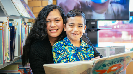 Adult and child smile at camera. Adult holds a book.