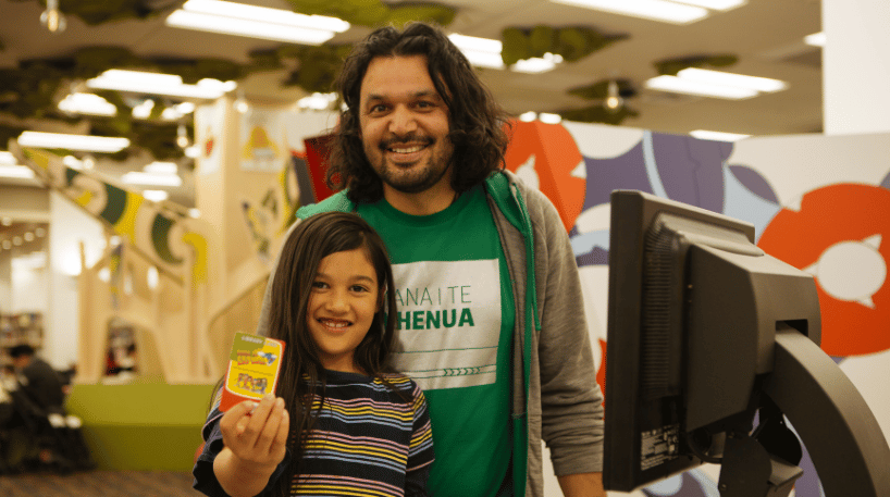 School-aged child and parent smiling with a new library card