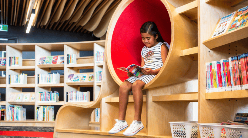Child reading a picture book in bright library furniture
