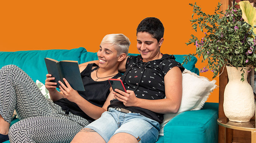 A couple, one reading a physical book and one reading on a mobile device.