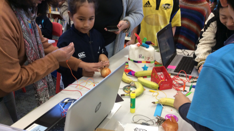 Image of several young children gathered around a table to learn how to use Makey Makey.