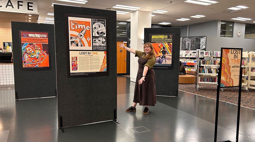 A librarian gestures toward large sci-fi illustration displays.