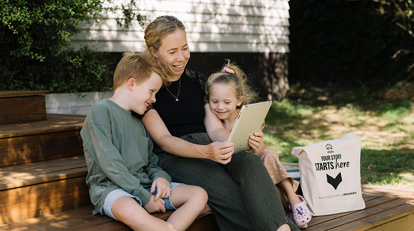 Photo of a lady with two children using a tablet outdoors
