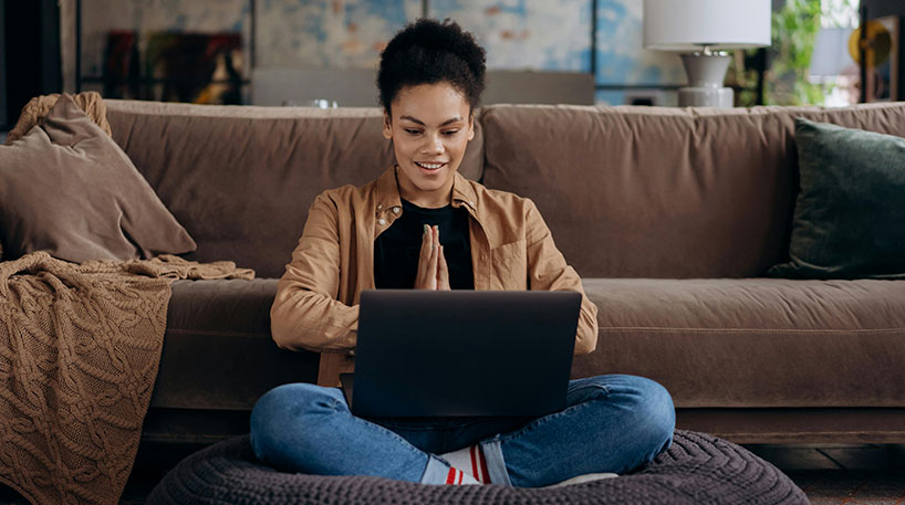 Young woman looking at laptop while sitting by a couch.