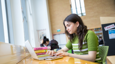 Photo of a student using a laptop in a library.