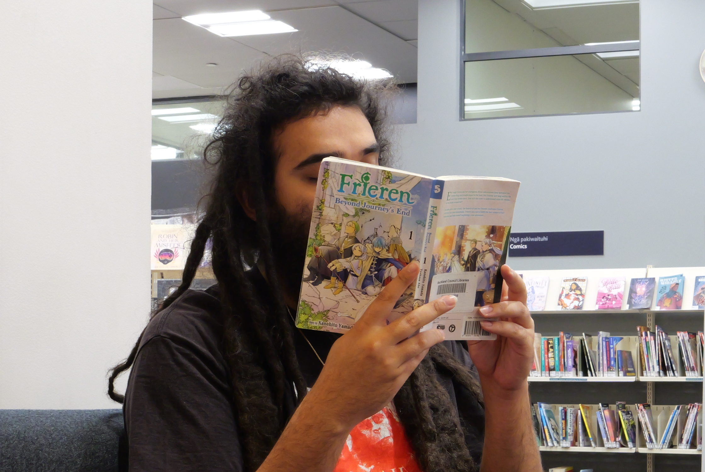 A man reading a manga titled 'Frieren' in the library.