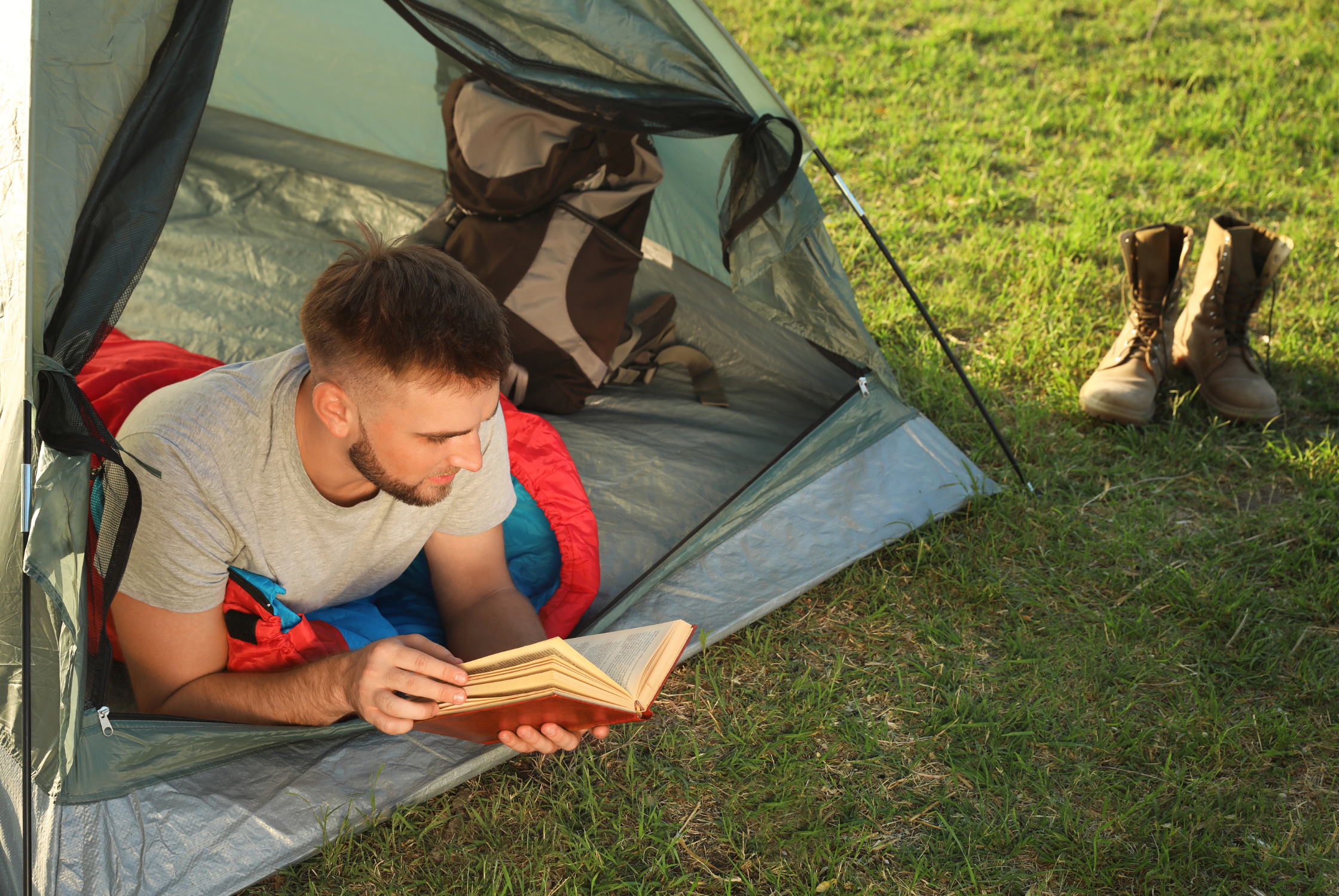 A young man reading in a tent entrance.
