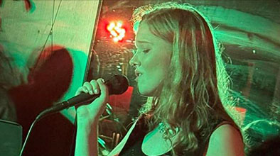 Photo of Ella Jean singing into a microphone under green and red lighting