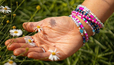 An open hand wearing beaded bracelets and touching daisy flowers.