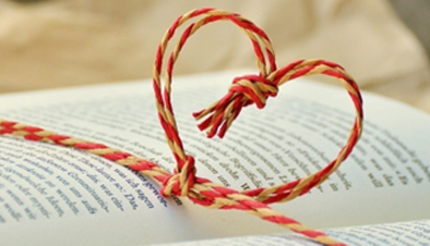 Red and white string knotted in heart shape above an open book.