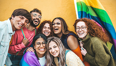 A group of young adults smiling and holding a rainbow flag.