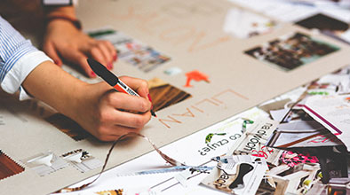 Close up of hand holding a pen above collage materials