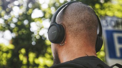 A man listening to headphones outdoors, facing away from the camera.