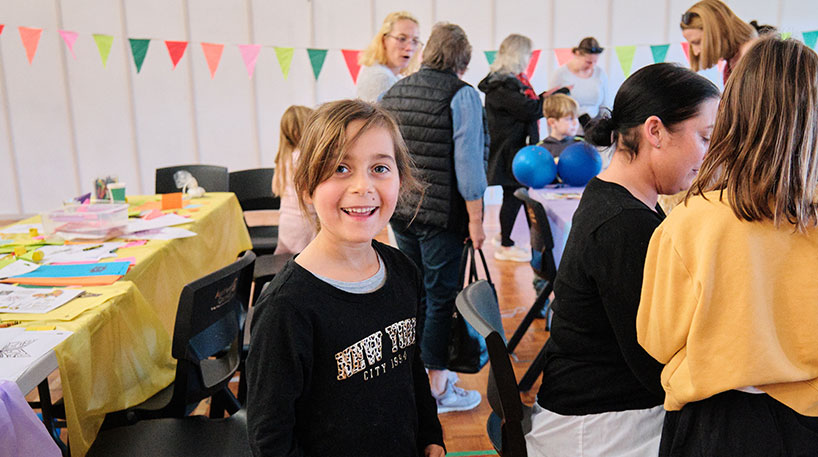 Young girl smiles in a hall of party-themed craft tables.