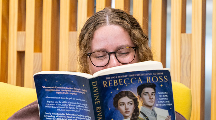woman reading Divine Rivals by Rebecca Ross
