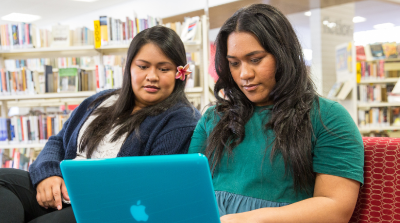 Two young women look at a laptop screen while visiting a library