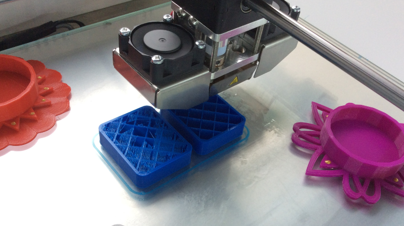 Image of a 3D printer printing rectangular blue shapes.